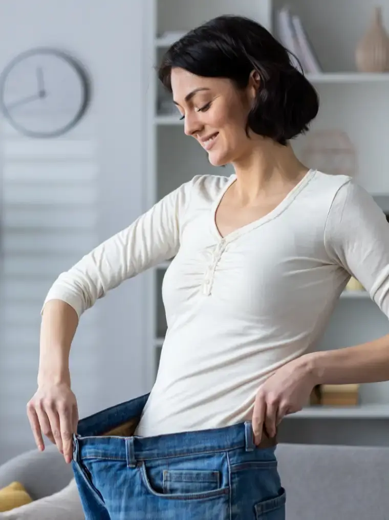 happy woman showing weight loss by wearing old jeans